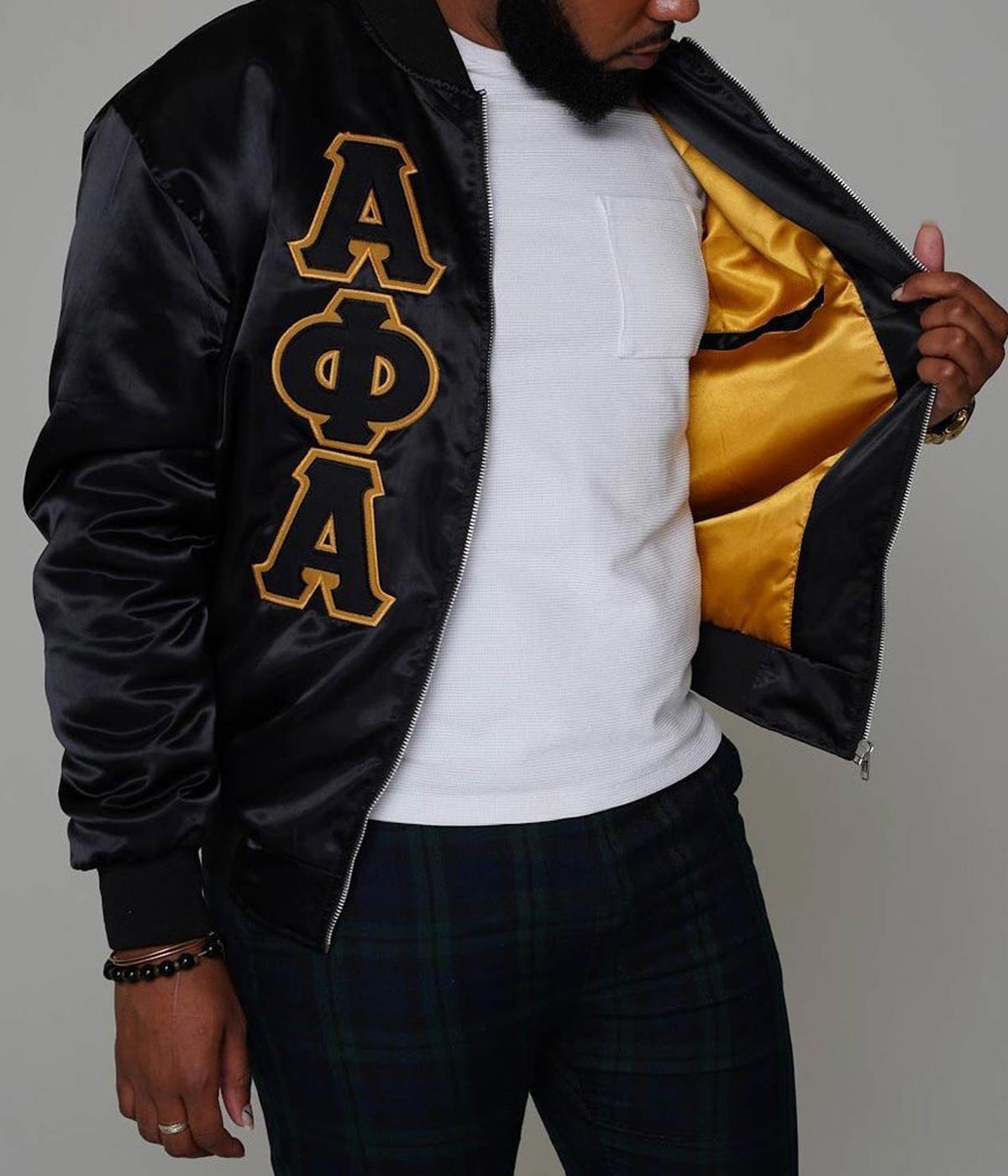 Black Alpha Phi Alpha bomber jacket held open to show yellow lining